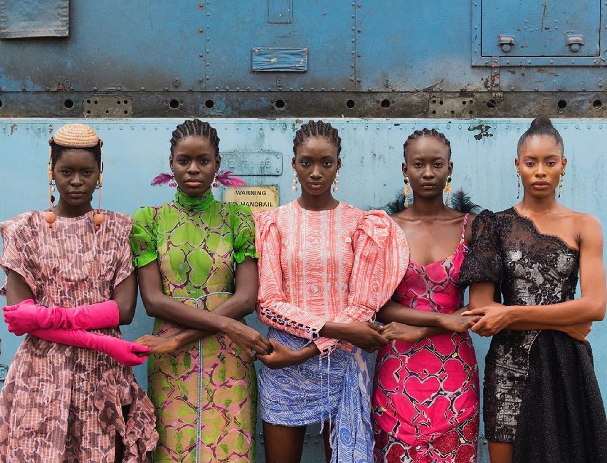 Cinq mannequins se tenant la main, vêtues de créations colorées issues de la mode africaine contemporaine